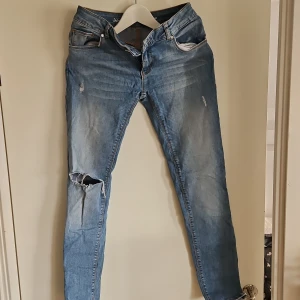 Blå jeans med slitningar - Snygga blå jeans med slitningar på knäet och lätt tvättad look. De har en klassisk femficksdesign och knappgylf. Perfekta för en avslappnad stil.