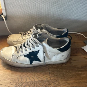 Golden Goose - Snygga vita sneakers från Golden Goose med en svart stjärna på sidan och svarta detaljer vid hälen. Skorna har snörning och en klassisk design som passar perfekt för en avslappnad stil.