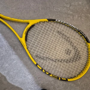 Gul tennisracket från Head - Säljer en gul tennisracket från Head, modell Titanium 2000. Racketen har ett svart och gult mönster med strängmönster 18M/19C. Perfekt för både nybörjare och erfarna spelare. Inkluderar ett svart fodral med Head-logga för enkel transport.
