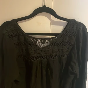 Svart blus med spetsdetaljer - Säljer en elegant svart blus med vackra spetsdetaljer vid halsringningen och ärmsluten. Blusen har långa ärmar och en lös passform, perfekt för en stilren look.
