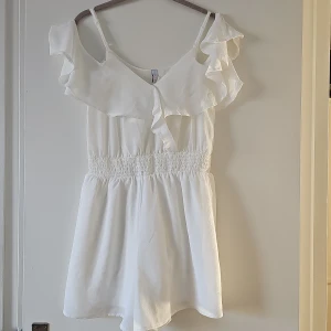 Vit jumpsuit från Amisu - Säljer en söt vit jumpsuit från Amisu i storlek S. Jumpsuit har volanger upptill och smala axelband. Den är tillverkad i polyester och har en elastisk midja för en bekväm passform. 