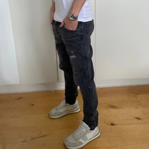 Svarta jeans med slitningar från Jack&Jones - Snygg svarta jeans med slitningar från Jack&Jones i Slim/Glenn modellen . Perfekta för en casual look med en vit t-shirt och sneakers. De har en klassisk design med fem fickor och knappgylf. Skick 9/10. Modellen är 177