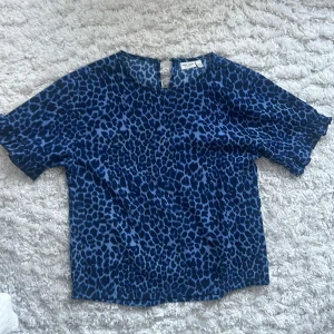 Blå leopardmönstrad topp från Basic Needs - Säljer en blå leopardmönstrad topp från Basic Needs. Toppen har korta ärmar och en avslappnad passform. Perfekt för en cool och trendig look. 🐆💙