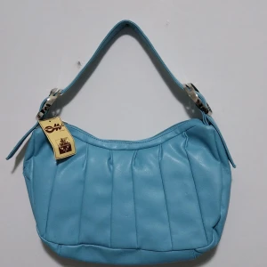 Blå axelväska från Maricci - Snygg blå axelväska från Maricci med justerbart axelband och silverdetaljer. Väskan har en dragkedja upptill och ett rymligt innerfack med extra ficka för småsaker. Perfekt för att bära med sig det viktigaste med stil.