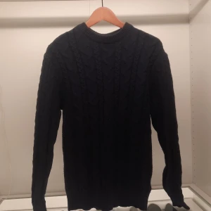 Svart stickad tröja från 157 - Säljer en svart stickad tröja från 157 i storlek S. Tröjan har ett klassiskt flätmönster och långa ärmar. Perfekt för kyligare dagar med sin mysiga och stilrena design.