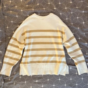Randig beige och vit tröja - Säljer en mysig randig tröja i beige och vitt. Tröjan har långa ärmar och en ribbad nederkant. Perfekt för en avslappnad stil. Med diskret slitt på sidan. Strlk 44(L) men passar S