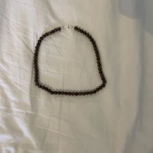Brunt pärlhalsband - Elegant halsband med bruna pärlor och ett silverfärgat lås. Perfekt för att ge en naturlig touch till din stil.