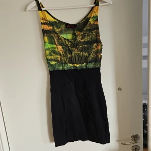 Färgglad klänning - Snygg klänning med ett färgglatt mönster i grönt, gult och orange upptill och en svart nederdel. Klänningen har en normal passform och ärmlös design, perfekt för sommarens varma dagar.