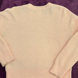 Rosa  stickad tröja - Säljer en mysig beige stickad tröja med rund hals och långa ärmar. Perfekt för kyligare dagar med ribbade muddar vid ärmslut och nederkant. En klassisk och stilren design som passar till det mesta.