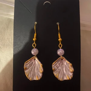 Guld- och pärlörhängen med snäckform - Egengjorda örhängen med guldfärgade krokar och snäckformade hängen. Varje örhänge har en vit pärla som detalj ovanför det snäckformade hänget. Perfekta för att ge en touch av havsinspiration till din stil.