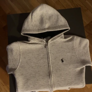 Vit zip hoodie från Ralph Lauren - Säljer en stilren vit hoodie från Ralph Lauren med dragkedja och snygg svart klädd huva. Tröjan har den klassiska loggan broderad på bröstet. Perfekt för en skön soft look men kan ändå va stilig med. köp av tröjan ger 25 lotter i tävlingen på våran Plick!!!