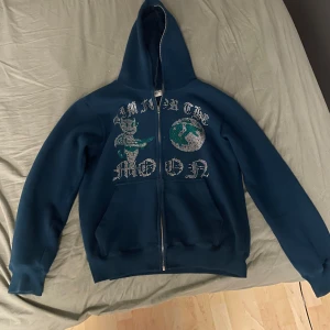 Mörkblå hoodie med tryck - En snygg fräsch Aim For The Moon hoodie! Storlek M, några paljett diamanter som har lossnat, inget man tänker på! Man tvättar den ut och in och i fintvätt! Skriv om några funderingar!