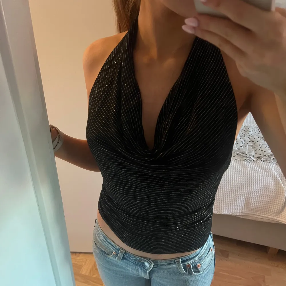Snygg svart halterneck topp med guldglittriga detaljer. Toppen har en djup urringning och öppen rygg. Perfekt för en kväll ute eller festliga tillfällen✨✨ Inga defekter. Yläosat.