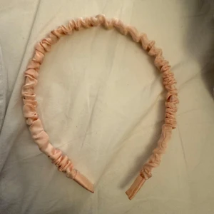Rosa diadem i satin - Säljer ett elegant rosa diadem i satin. Diademet har en rynkad design som ger en fin textur och stil. Perfekt för att lägga till en touch av färg och elegans till din outfit.