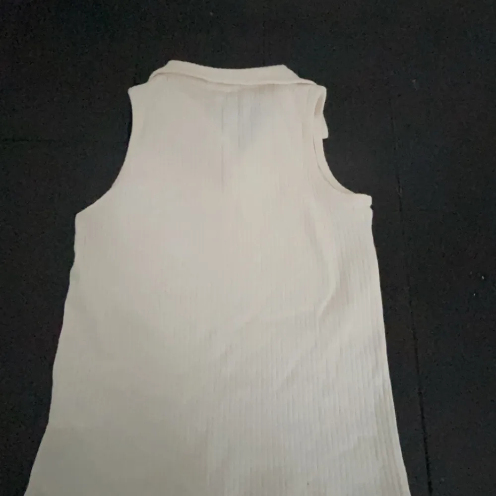 Säljer en stilren vit ärmlös topp från H&M. Toppen har en ribbad struktur och en liten krage med v-ringning. Perfekt för varma dagar eller som ett lager under en jacka.. Yläosat.