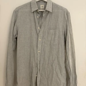 Grå skjorta från H&M - Säljer en stilren grå skjorta från H&M med långärmad design och klassisk krage. Skjortan har knappar framtill och en bröstficka. Perfekt för en avslappnad men ändå uppklädd look.