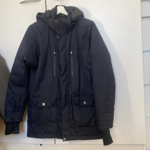 Svart vinterjacka med huva från Everest  - Säljer en svart vinterjacka med huva och dragkedja. Jackan har långa ärmar och praktiska fickor med knappar framtill. Stl 164 ( small)