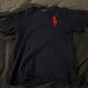 Mörkblå t-shirt från Ralph Lauren - Säljer en mörkblå t-shirt från Ralph Lauren med röd broderad logga på bröstet. T-shirten är kortärmad och tillverkad i bomull. Passar perfekt för vardagen. Priset är ej hugget i sten och kan diskuteras i en snabb affär.