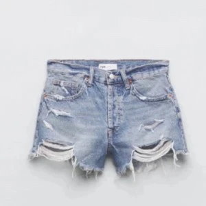 Blå jeansshorts från Zara - Snygga blå jeansshorts från Zara med slitna detaljer och fransiga kanter. Perfekta för en avslappnad stil. De är högmidjade och har en klassisk femficksdesign.