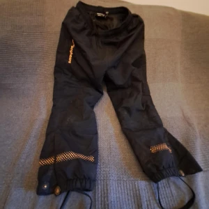Svarta täckbyxor från Bagheera (barn) - Säljer ett par svarta täckbyxor från Bagheera. Byxorna har elastiska benslut med justerbara remmar och tryckknappar. Perfekta för utomhusaktiviteter under kalla dagar.