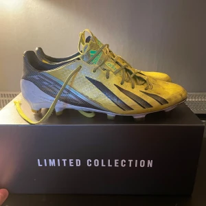 adidas F50 - Snygga gula fotbollsskor från Adidas Limited Collection med svarta detaljer och snörning. Skorna har en modern design med en lätt och smidig passform, perfekt för snabba rörelser på planen.