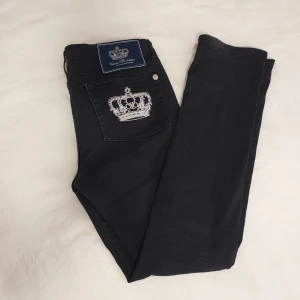 Svarta Victoria beckham jeans - Lågmidjade svarta jeans med en broderad krona på bakfickan. De har en lite utsvängd modell. Säljer då de är för stora (strl 28). Midjemått - ca 42 och Innerbenslängd - ca 76