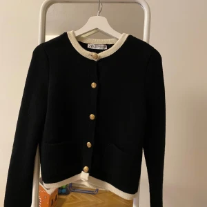 Svart cardigan från Zara stl m - Snygg svart cardigan  från Zara med guldfärgade knappar och vita detaljer vid krage och ärmslut. Stl M, liten i stl så passar även S.                                         Helt oanvänd! Passade tyvärr inte mig 💞