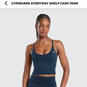 Mörkblå cami tank från Gymshark - Snygg mörkblå cami tank från Gymshark med smala axelband och en croppad passform. Perfekt för träning eller en avslappnad dag. Den har en enkel design med en liten logga på bröstet.