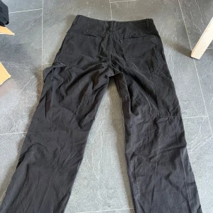 Lågmidjade cargobyxor från Bershka - Snygga svarta lågmidjade  cargobyxor från Bershka med en klassisk design. Byxorna har en knapp och dragkedja framtill samt praktiska fickor. Väldigt lite använda av mig, som nya. 