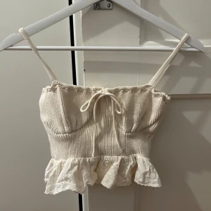 Beige ribbad linnetopp med volang - Söt beige ribbad linnetopp med smala axelband och volangdetalj nedtill. Toppen har en knytning framtill som ger en fin detalj💞💞storlek s men mer som en xs