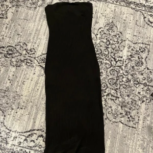 Svart axelbandslös klänning - Snygg svart axelbandslös klänning som passar perfekt för en kväll ute. Den har en tight passform som framhäver figuren och är gjord i ett mjukt material för extra komfort.