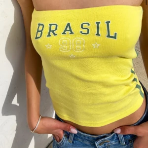 Gul tubtopp med Brasil-tryck - Snygg gul tubtopp med texten 'BRASIL 98' i grönt och vitt. Perfekt för en somrig look med en sportig touch. Toppen är ärmlös och har en tight passform.
