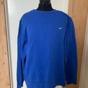 Blå långärmad tröja från Nike - Säljer en snygg blå långärmad tröja från Nike med en liten vit logga på bröstet. Perfekt för en avslappnad stil. Tröjan har ribbade muddar vid ärmslut och nederkant.