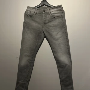 Grå jeansbyxor ifrån G Star  - Snygga grå jeansbyxor med en klassisk femficksdesign. De har en rak passform och är perfekta för en stilren look. Byxorna har en knappgylf och bälteshällor.