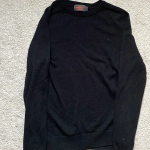 Svart merinoull  tröja från Morris - Säljer en stilren svart tröja från Morris i 100% merinoull. Tröjan har en diskret broderad logga på bröstet och långa ärmar. Perfekt för en elegant och bekväm look.