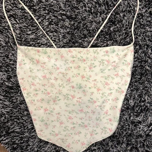 Blommig topp💐 - Söt topp med blommigt mönster i rosa och grönt i ett silkes tyg!! Toppen har tunna axelband och en knytning i ryggen för en justerbar passform. Den är endast provad så den är i nyskick! Perfekt för varma sommardagar 💌