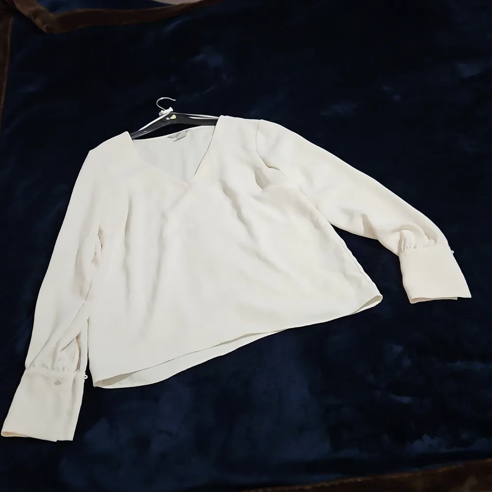Säljer en stilren vit blus från H&M i storlek 38. Blusen har långa ärmar med knappar vid ärmsluten och en v-ringad hals. Perfekt för en elegant look.. Puserot.