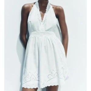 Vit klänning med spetsdetaljer - Säljer en söt vit klänning med spetsdetaljer och halterneck-design. Klänningen har en v-ringad fram och knytning i nacken. Perfekt för sommarens varma dagar! Helt oanvänd med prislapp kvar💗nypris 700kr