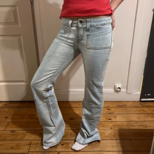 Ljusblå bootcut jeans lågmidjade  - Snygga ljusblå bootcut jeans med låg midja och klassisk femficksdesign. Perfekta för en avslappnad stil med en touch av retro. De har en dragkedja och knapp framtill.