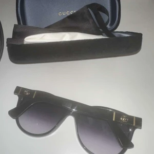 Svarta solglasögon från Gucci - Snygga svarta solglasögon från Gucci med en elegant design. De har en bred båge och mörka glas som ger ett stilrent intryck. Perfekta för att ge en lyxig touch till din outfit.