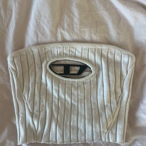 Vit ribbad tubtopp med metalllogo Diesel - Säljer en stilren vit ribbad tubtopp med en  metallogo Diesel framtill. Toppen är axelbandslös och har en tight passform som framhäver figuren..