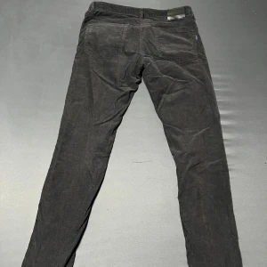 Svarta manchesterbyxor från Gant - Snygga svarta manchesterbyxor från Gant i slim fit. Byxorna har en klassisk design med knappar och dragkedja framtill. Perfekta för en stilren look. 31/34