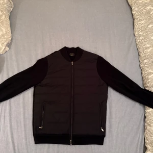 Massimo Dutti cardigan - Snygg svart cardigan från Massimo Dutti med dragkedja framtill och ribbade muddar. Jackan har långa ärmar och två fickor med dragkedja. Perfekt för en stilren look. Använt ett fåtal gånger men ser ut som ny. Den är för stor för mig som ni ser på bilden då jag brukar ha M