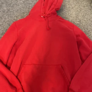 Röd hoodie från 157 - Säljer en klassisk röd hoodie från 157. Den har en justerbar huva med dragsko och en stor magficka framtill. Perfekt för en avslappnad stil.