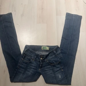 Blå jeans från Bershka - Snygga blå lågmidjade jeans från Bershka med en klassisk femficksdesign och dubbla knappar i midjan. Jeansen har en lätt slitning för en trendig look och är perfekta för en avslappnad stil💕