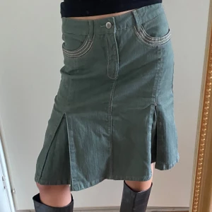 Militärgrön veckad kjol - Knälång militärgrön/olivgrön kjol med fram- och bakfickor. Tjockt bomullsmaterial som liknar jeanstyg. Köpt second hand, använd fåtal gånger.