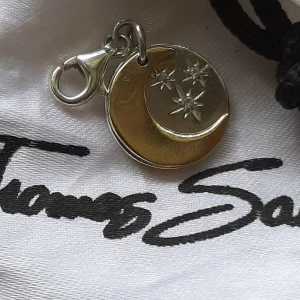 Silver- och guldfärgad berlock från Thomas Sabo - Thomas Sabo berlock av en bricka m sol o måne i både silver och guld, är i fint begagnat skick. Kolla bilder o ställ ev frågor före bud. Ask/påse ingår ej. 