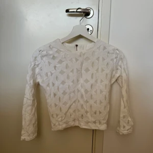 Vit spetsmönstrad topp med dragkedja - Säljer en superfin vit topp med spetsmönster och lång ärm. Den har en dragkedja i ryggen för en snygg detalj och enkel påklädning. Perfekt för vår och sommar, och funkar både till vardags och fest. Toppen är använd och har lite makeup på halsen. Passar perfekt till jeans eller kjol för en chic look!