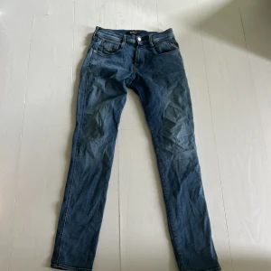 Blå jeans från Replay - Säljer ett par snygga blå jeans från Replay. De är i storlek 27/32 och har en klassisk femficksdesign med dragkedja och knapp. Jeansen är i bra skick och har en straight passform. Perfekta för både vardag och fest!