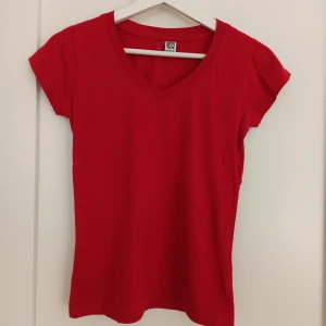 Röd t-shirt från Roly - Säljer en snygg röd t-shirt från Roly i storlek S. Den är gjord av bomull och är v-ringad🌟 Passar till allt! T-shirten är i nyskick förutom en minimal fläck som syns på sista bilden. inte provat att ta bort. Passformen är mer åt det figurnära hållet och den är superbekväm att ha på sig. Köp den nu och ge din garderob en färgklick! ❤️
